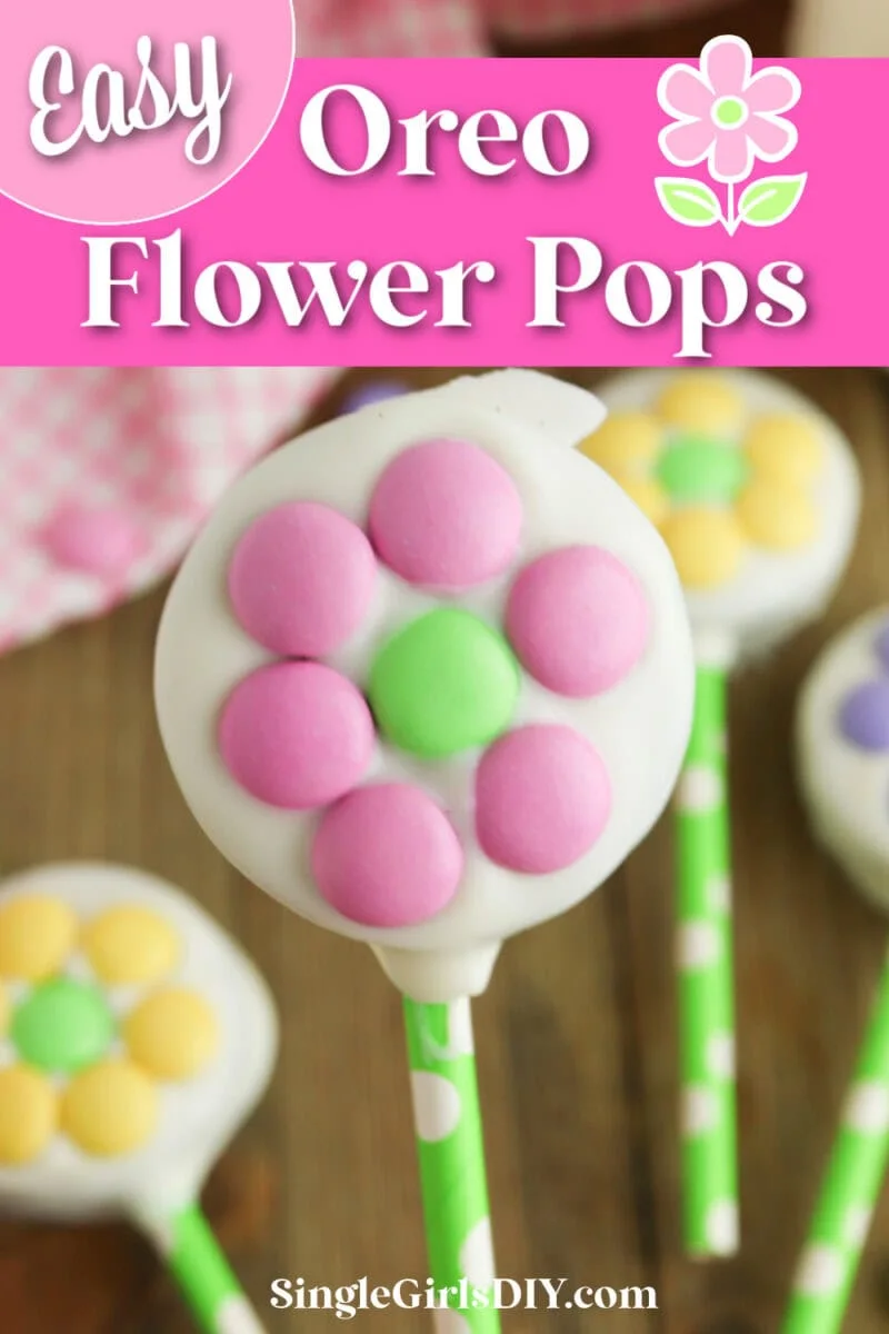 A cookie pop decorated with pink and green flower-shaped candy on a green polka dot stick. Background shows more similar pops. Text reads "Easy Oreo Flower Pops".