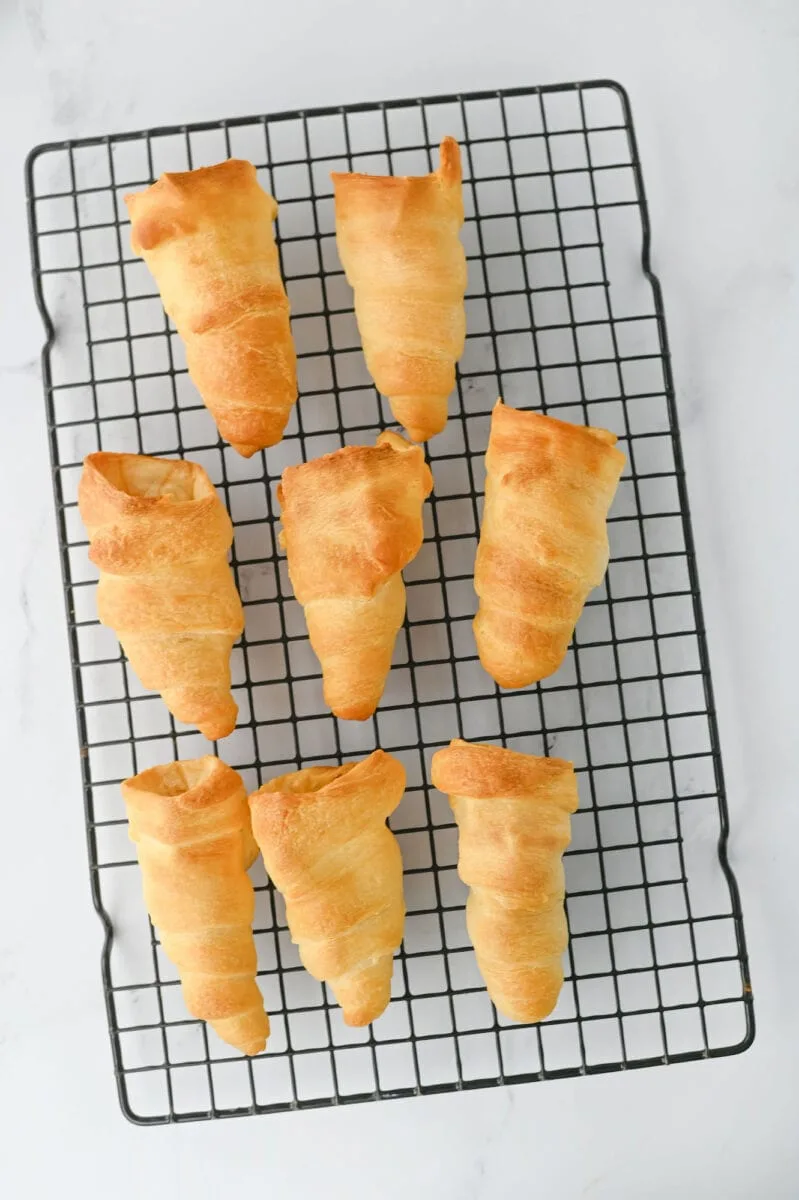 Seven golden-brown croissants cooling on a wire rack on a white surface.