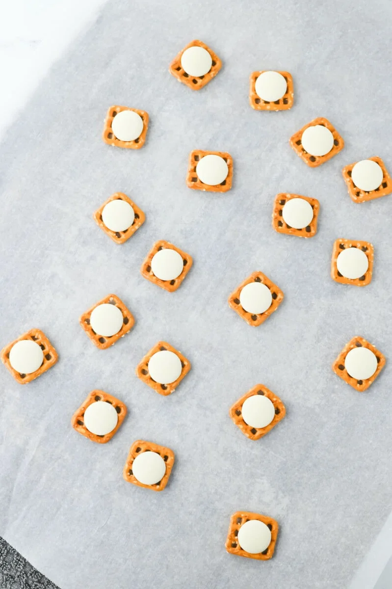 Square pretzels with round white chocolates on top are arranged on parchment paper, creating delightful Easter bunny pretzel treats.