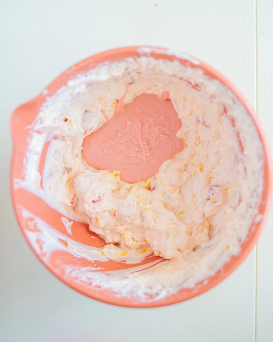 A mixing bowl with partially mixed pink and white creamy contents on a light-colored surface.