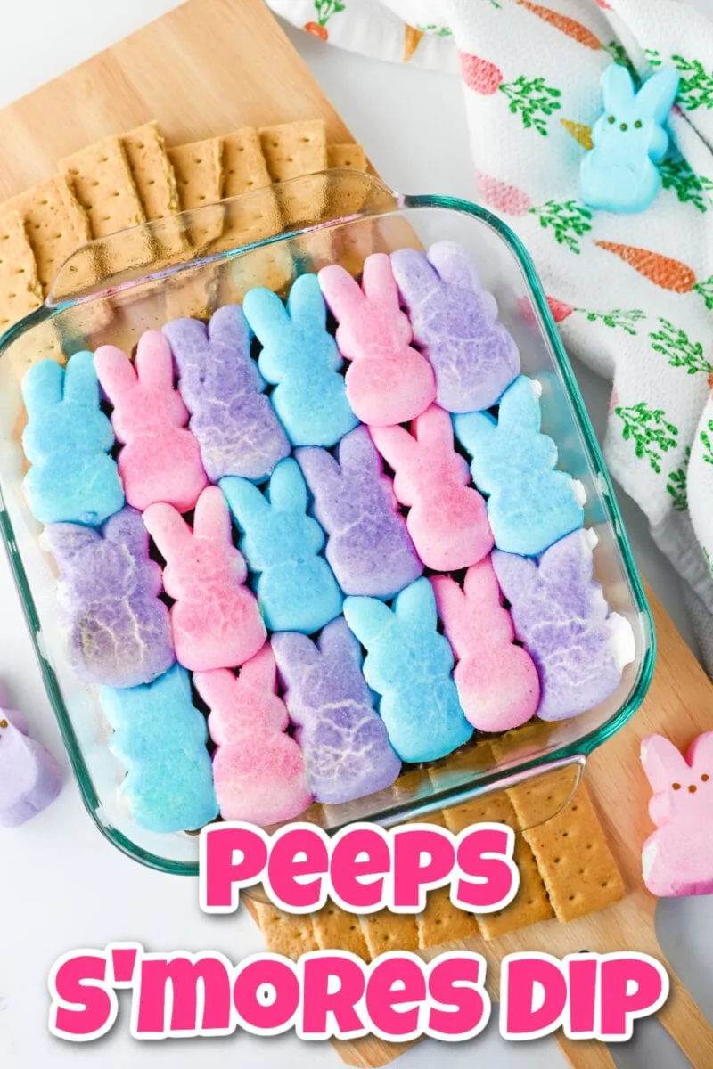 A glass dish with layers of blue, pink, and purple marshmallow bunnies on chocolate, labeled "Peeps S'mores Dip." Crackers are placed nearby on a wooden board.