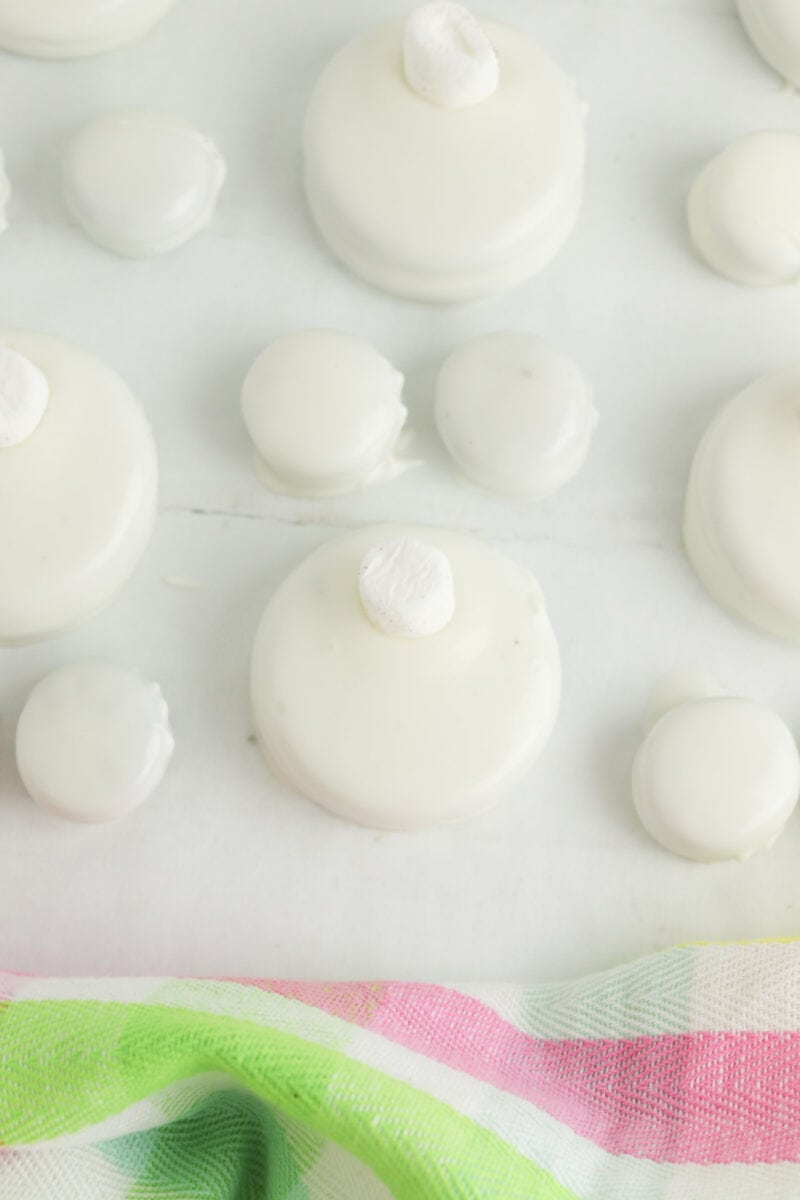 White chocolate-covered cookies and smaller round treats with a dollop on top, arranged on parchment paper. A striped fabric is partially visible at the bottom.