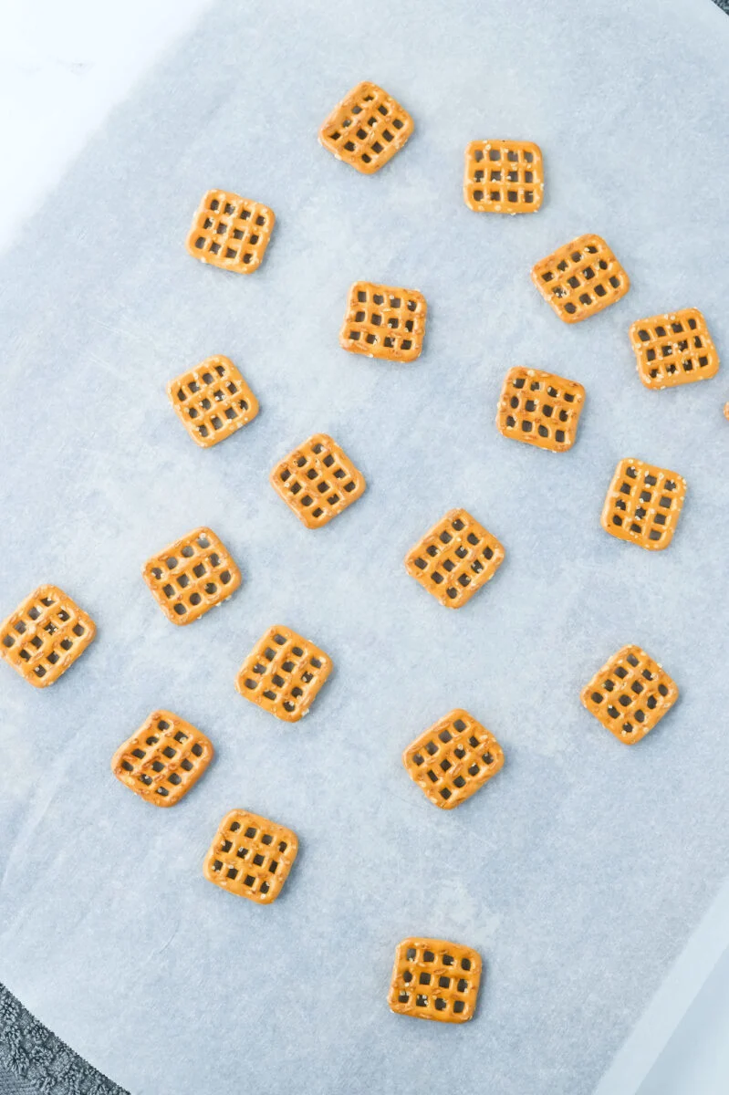 Square pretzels, perfect for Easter bunny pretzel treats, are evenly spread out on a sheet of parchment paper.