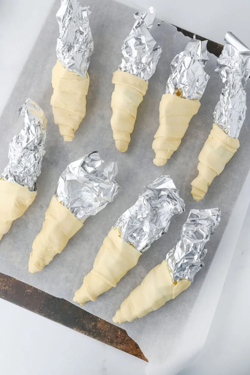 Unbaked pastry cones wrapped in foil on a baking sheet lined with parchment paper.