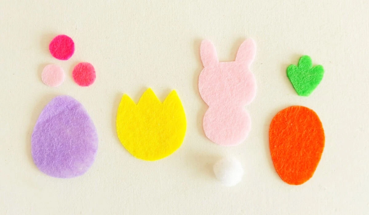 Felt shapes on a white background, including a purple egg, yellow flower, pink bunny, orange carrot, and small pink, white, and green circles.