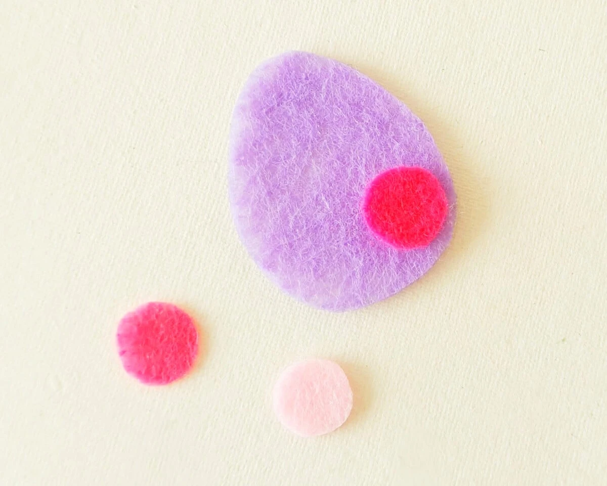 Purple felt teardrop shape with a small pink circle on it, and two more pink circles in varying shades on a light background.