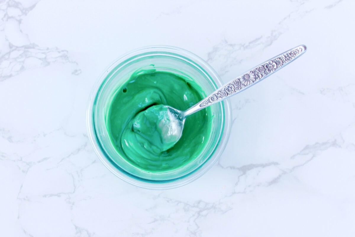 A bowl of green yogurt with a spoon on a marble surface.