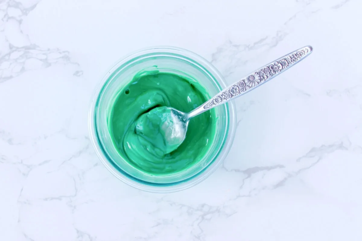 A bowl of green yogurt with a spoon on a marble surface.