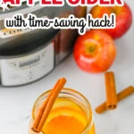Jar of crockpot apple cider with cinnamon sticks and orange slice in front of a crockpot and apples, with text: “Warm and cozy crockpot apple cider with time-saving hack!”.