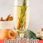 A champagne flute filled with apple cider mimosa, garnished with a rosemary sprig, cinnamon stick, and apple slice. Text overlay reads “Apple Cider Mimosa.”.