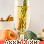 A champagne flute filled with apple cider mimosa, garnished with a rosemary sprig, cinnamon stick, and apple slice. Text overlay reads “Apple Cider Mimosa.”.