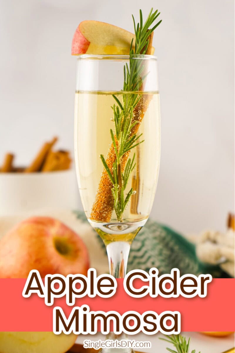 A champagne flute filled with apple cider mimosa, garnished with a rosemary sprig, cinnamon stick, and apple slice. Text overlay reads “Apple Cider Mimosa.”.