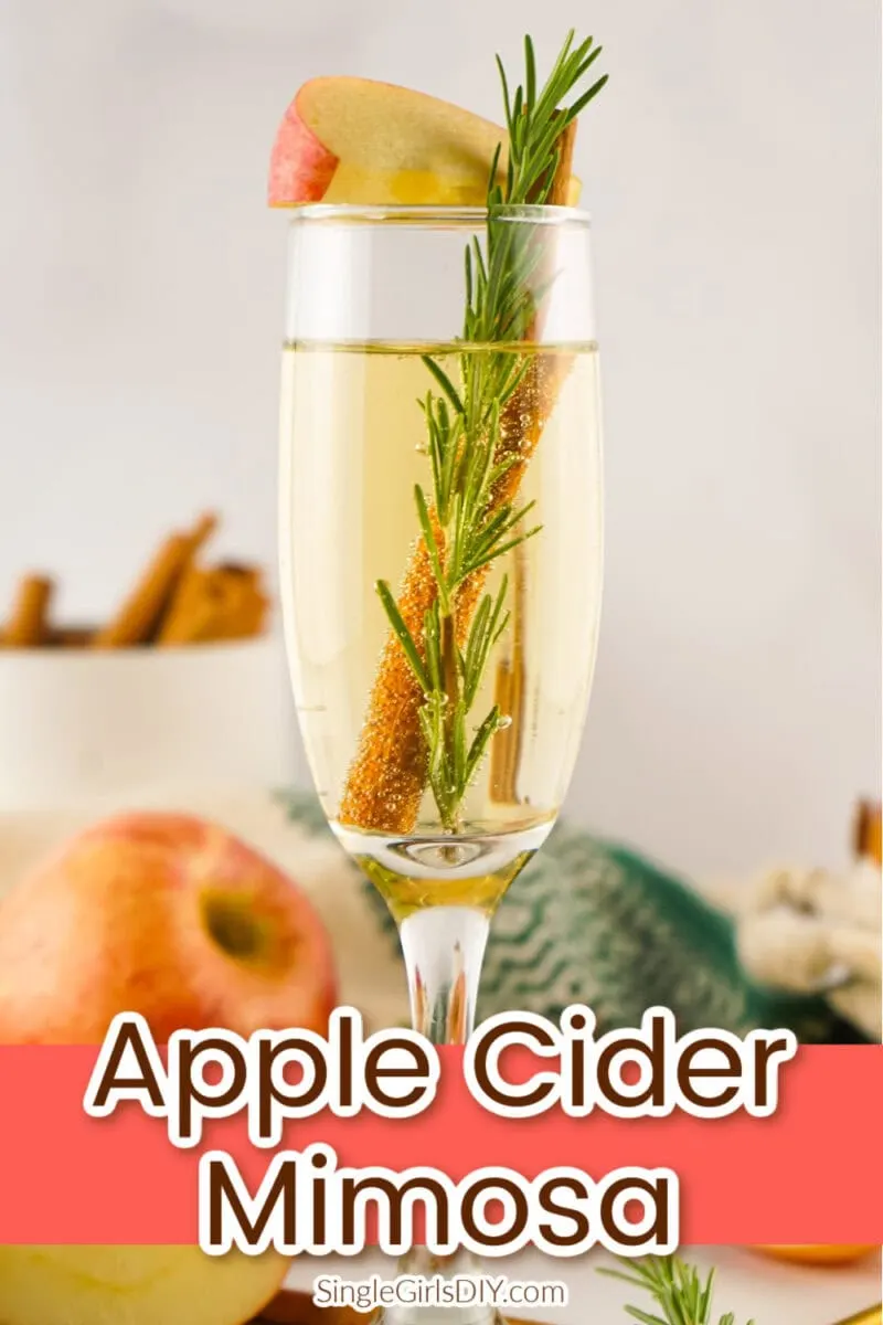 A champagne flute filled with apple cider mimosa, garnished with a rosemary sprig, cinnamon stick, and apple slice. Text overlay reads “Apple Cider Mimosa.”.