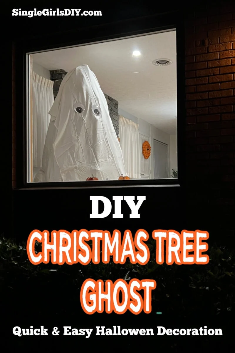 A white sheet with cut-out eyes draped over a Christmas tree creates a ghost figure in a window, promoting a DIY Halloween decoration idea.