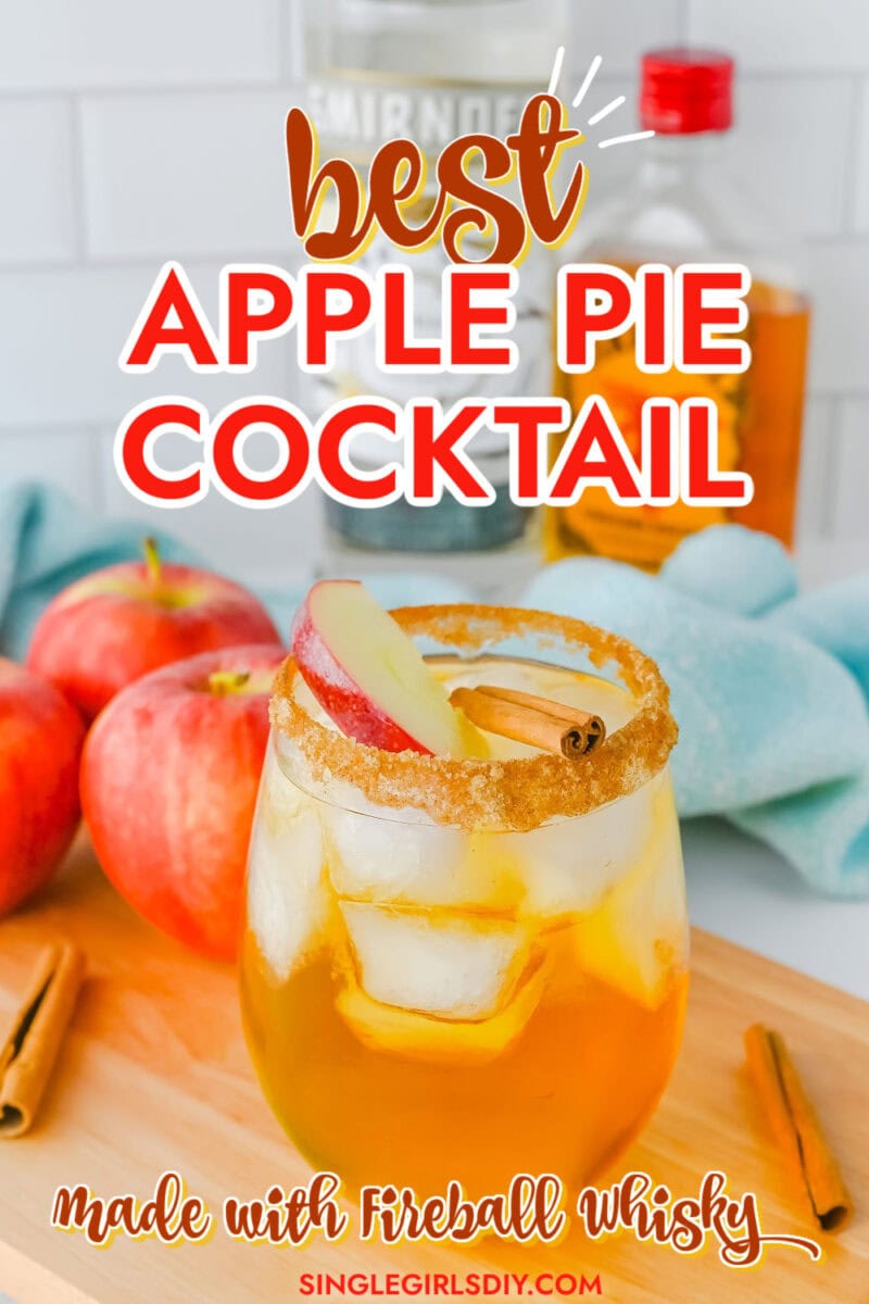 A glass of apple pie cocktail with ice, garnished with apple slices and a cinnamon stick, sits on a wooden surface next to fresh apples and cinnamon sticks. Discover the bold flavor of Fireball Whisky in every sip of this apple pie cocktail.