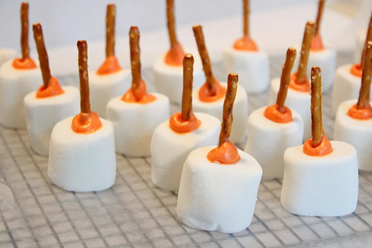 Pumpkin patch marshmallow treats with orange icing and pretzel sticks in the center, arranged on a wire cooling rack.