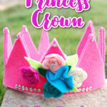 A pink felt princess crown decorated with fabric flowers and rhinestones, displayed outdoors with text promoting a DIY tutorial and free template from SingleGirlsDIY.com.