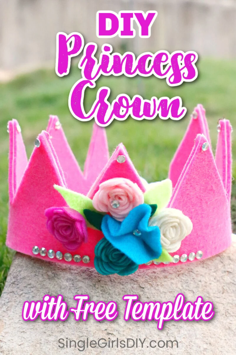 A pink felt princess crown decorated with fabric flowers and rhinestones, displayed outdoors with text promoting a DIY tutorial and free template from SingleGirlsDIY.com.