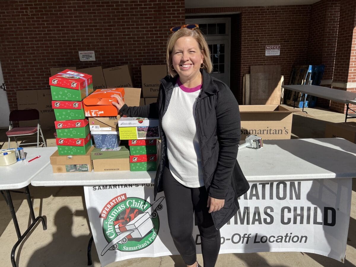 A woman stands next to a table with boxes, preparing them for Operation Christmas Child.