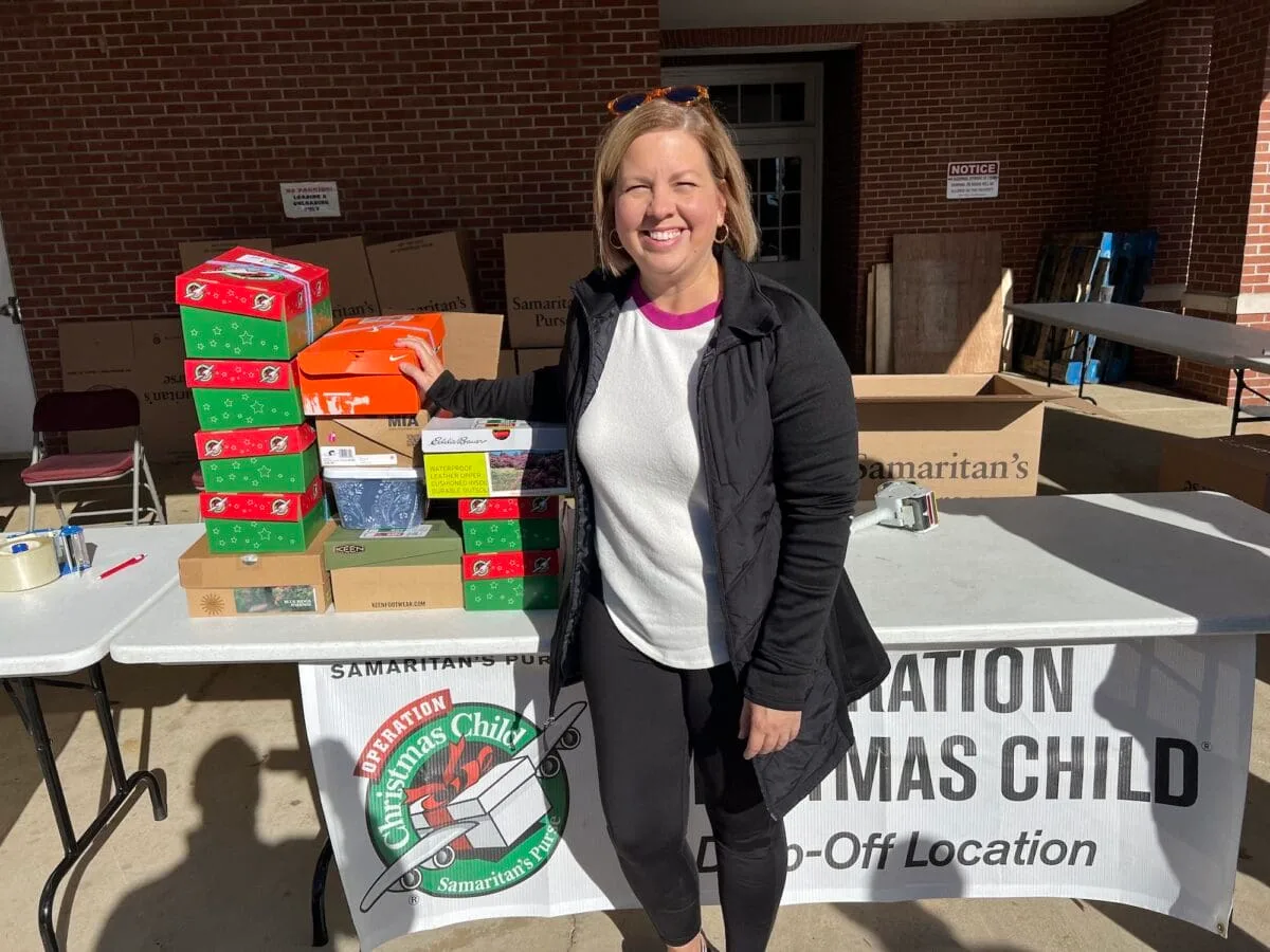 A woman stands next to a table with boxes, preparing them for Operation Christmas Child.