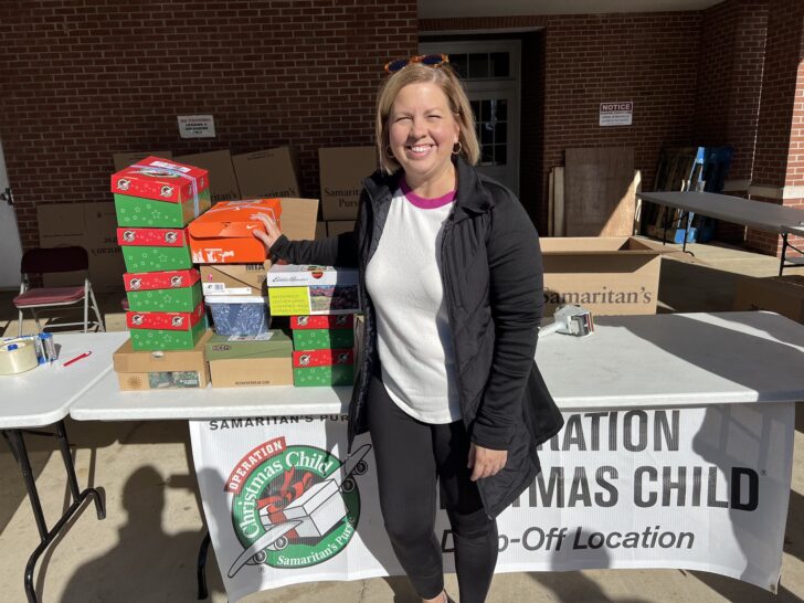 A woman stands next to a table with boxes, preparing them for Operation Christmas Child.