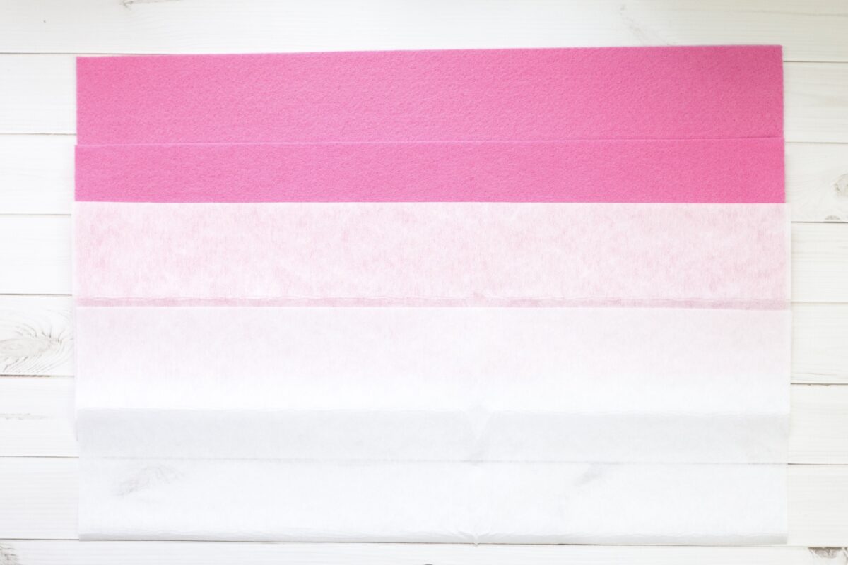 Four large sheets of tissue paper in descending shades from bright pink at the top to white at the bottom, laid out on a white wooden surface.