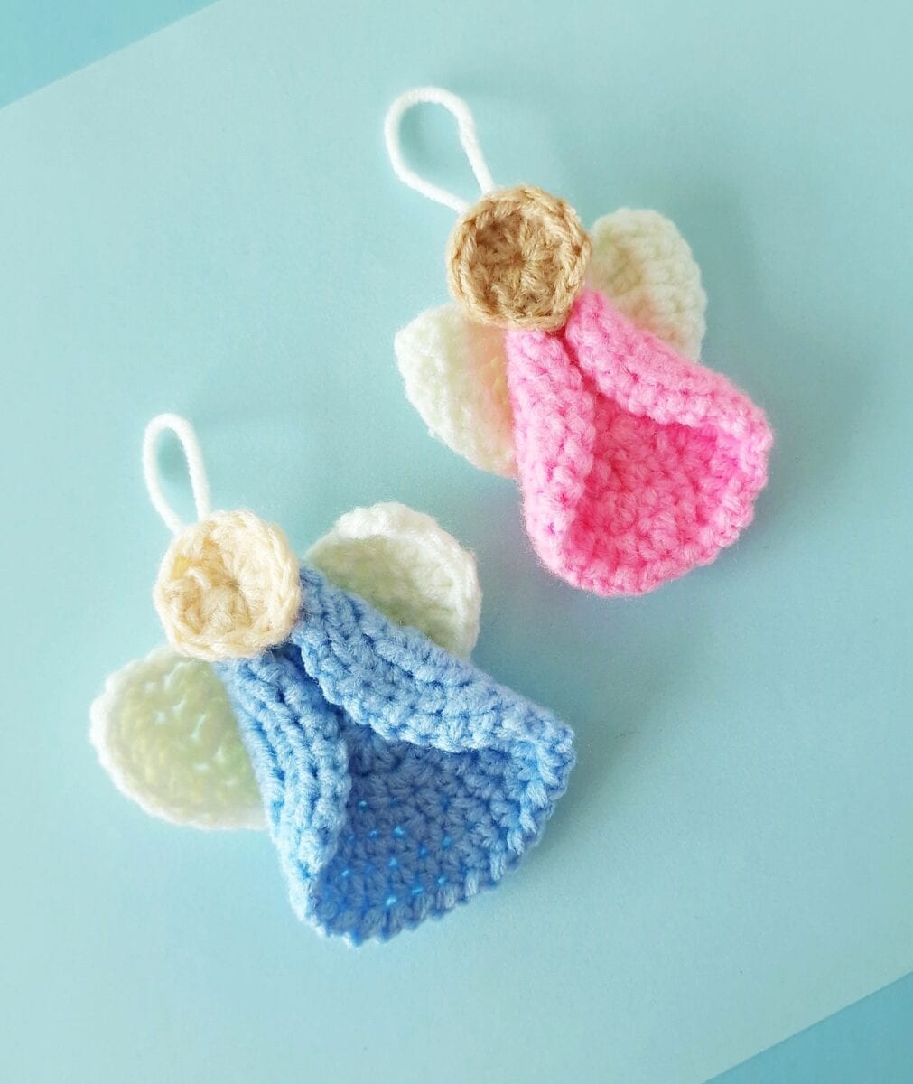 Two crocheted angel ornaments with wings, one in blue and one in pink, are placed on a light blue background.