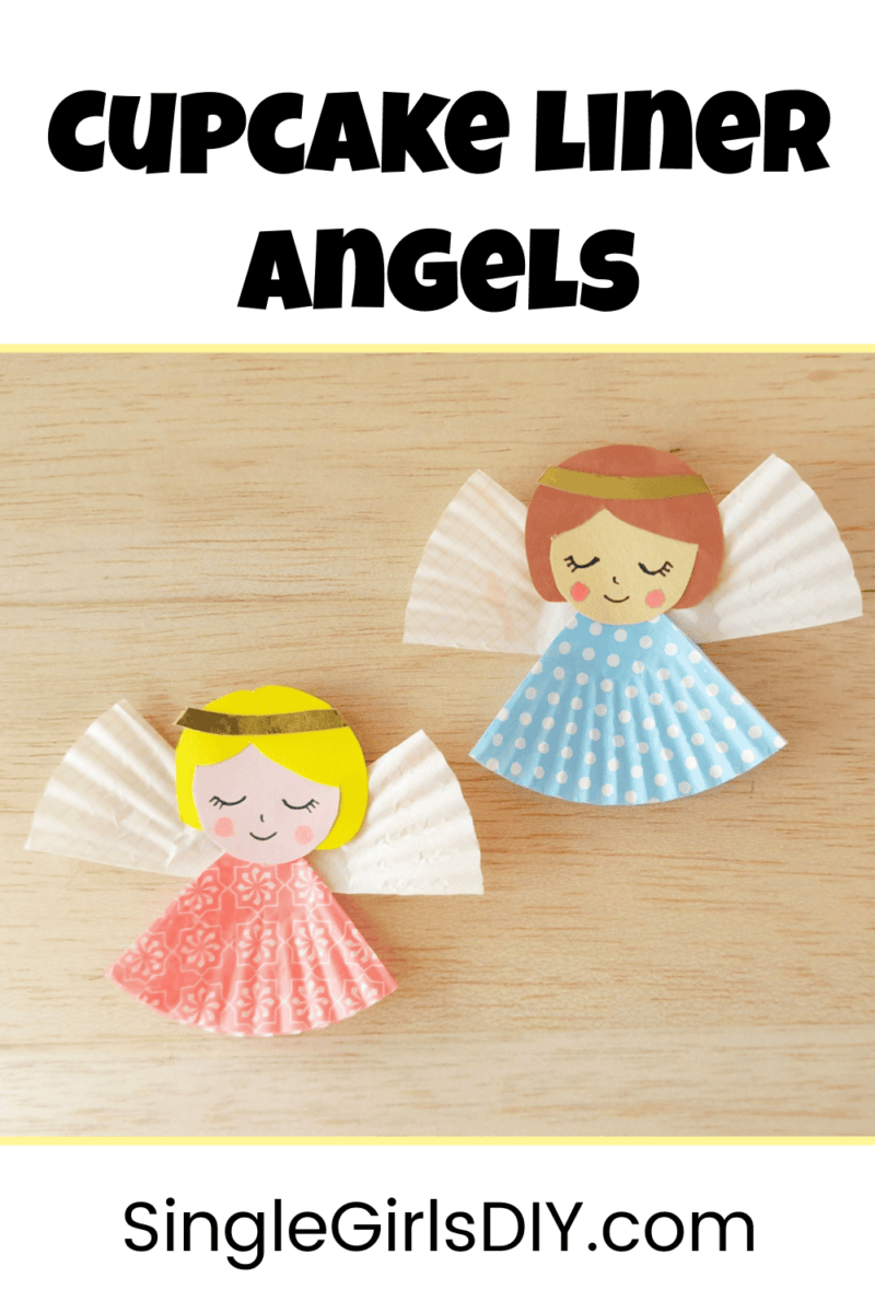 Two paper angels made from cupcake liners with drawn faces and golden hairbands, one in pink and one in blue, displayed on a wooden surface.