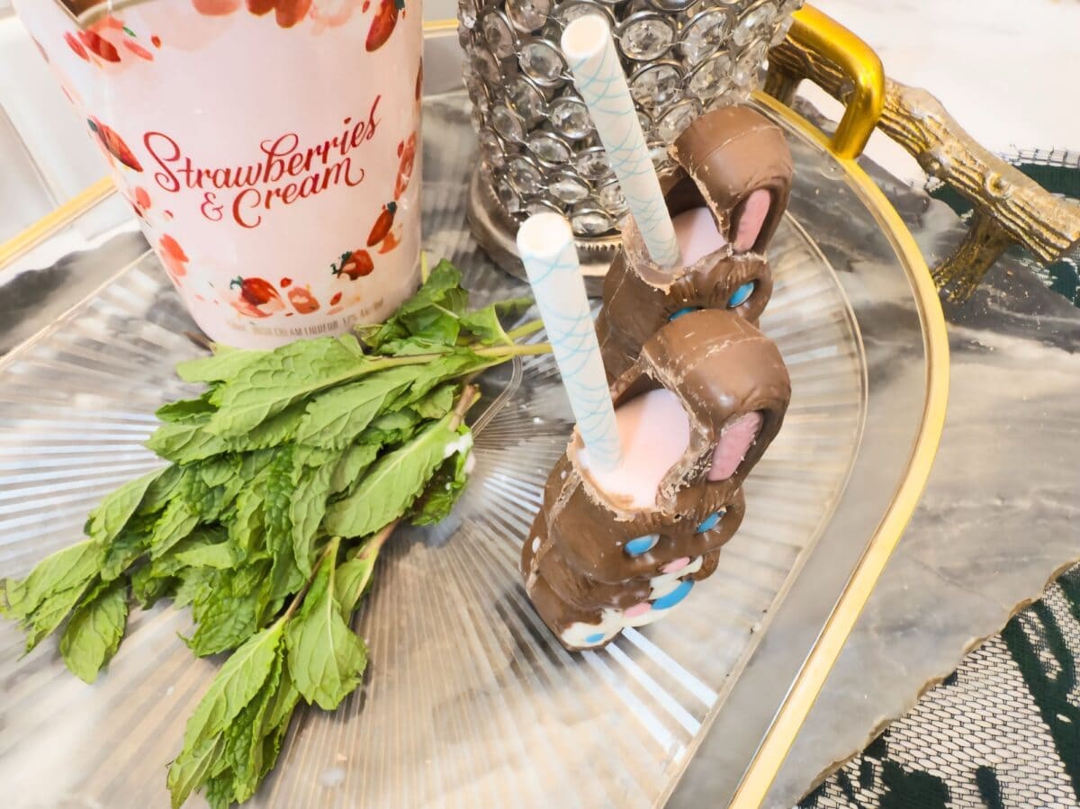 A glass tray holding a bunch of mint, two chocolate rabbit cocktail treats with straws, and a cup labeled "Strawberries & Cream.