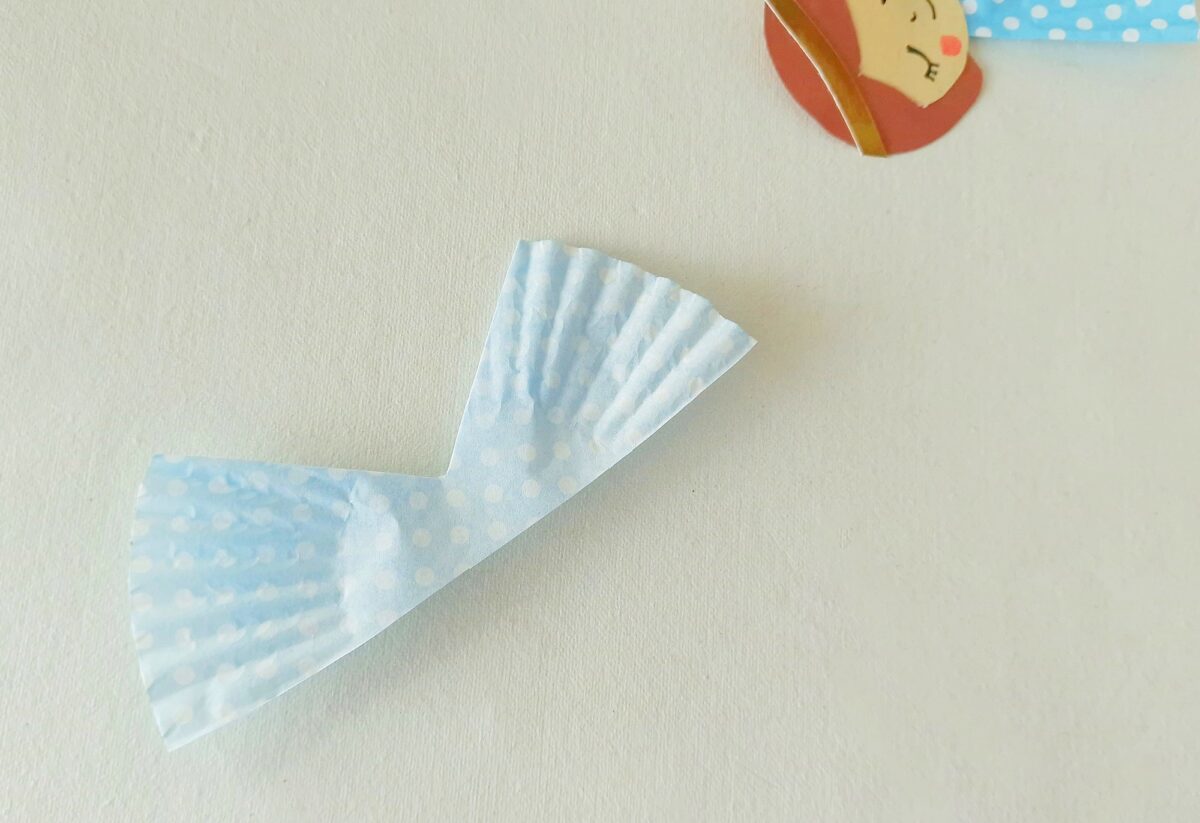 A light blue, polka-dotted cupcake liner is folded and placed on a white surface, with a partial illustration of a face visible in the corner.