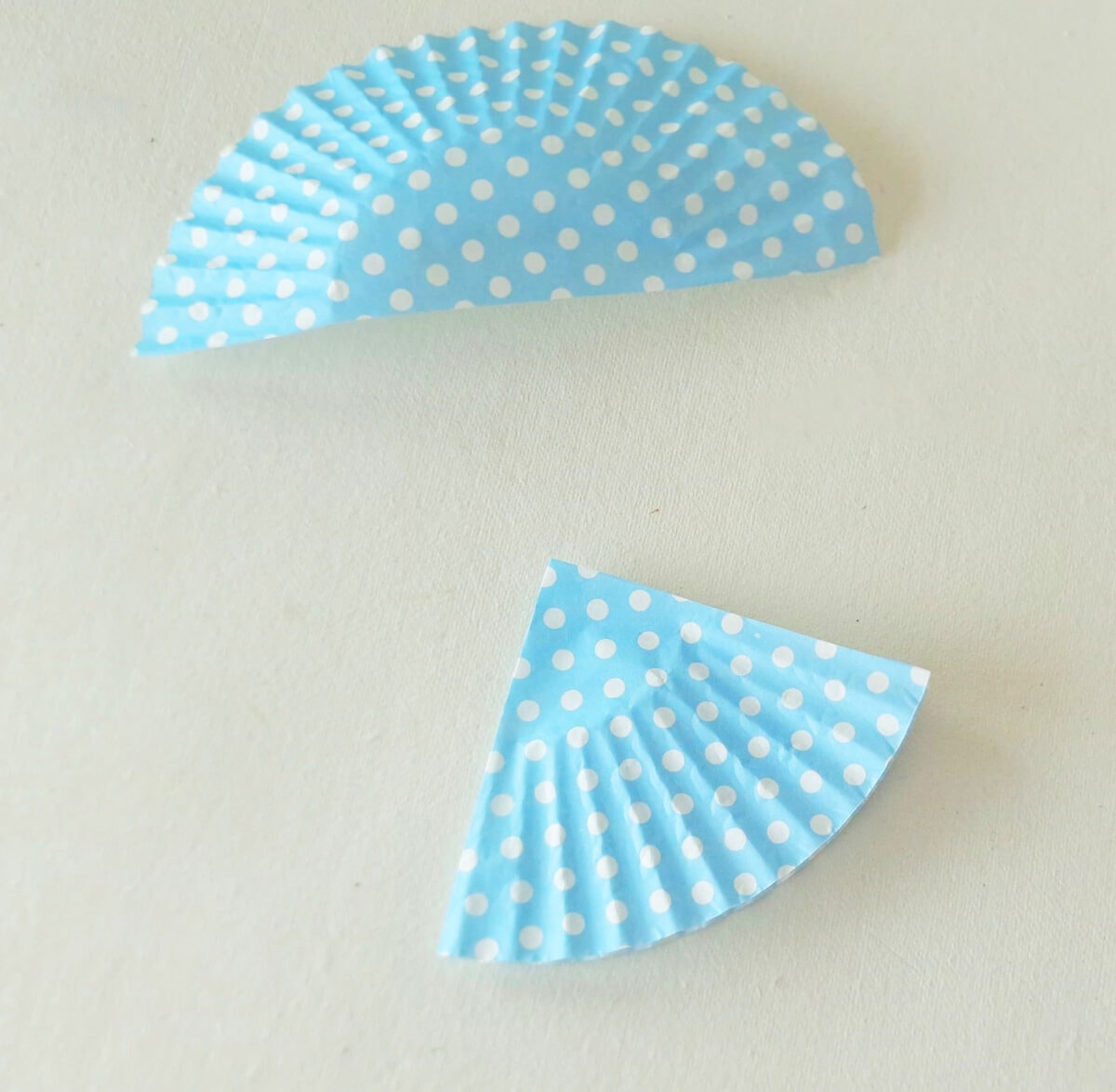 Two blue paper cupcake liners with white polka dots are folded in half and placed on a white surface, one intact and one with a quarter section cut out.