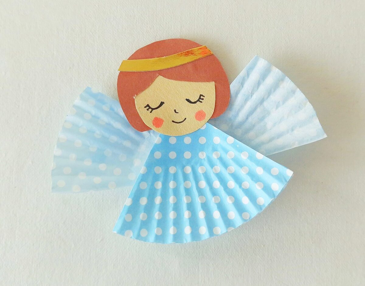 A paper angel craft with a round face, short brown hair, a gold headband, and a blue polka dot dress and wings made from cupcake liners.