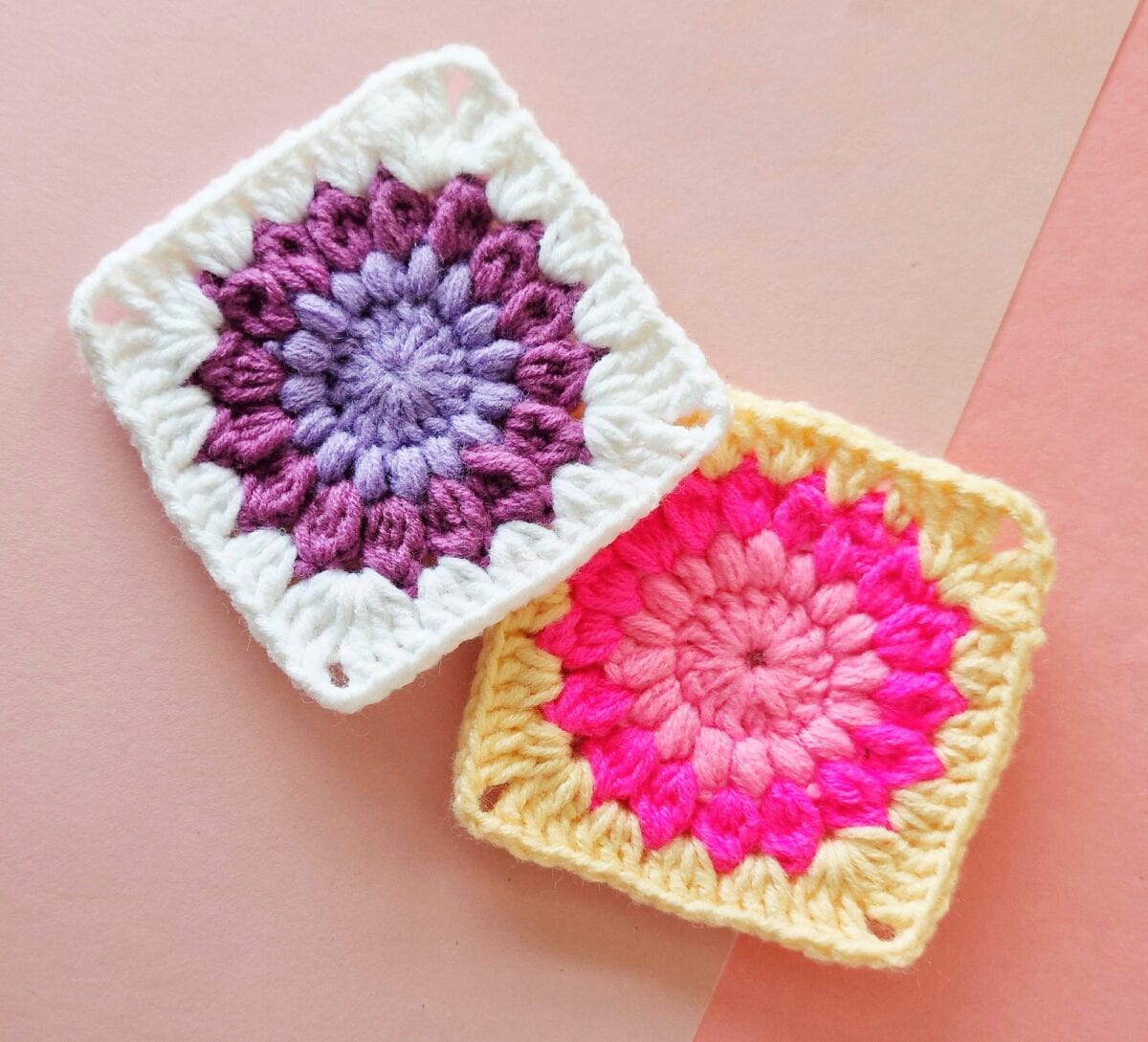 Two colorful crocheted granny squares, one with purple and white yarn and the other with pink and yellow yarn, placed overlapping on a pink background.