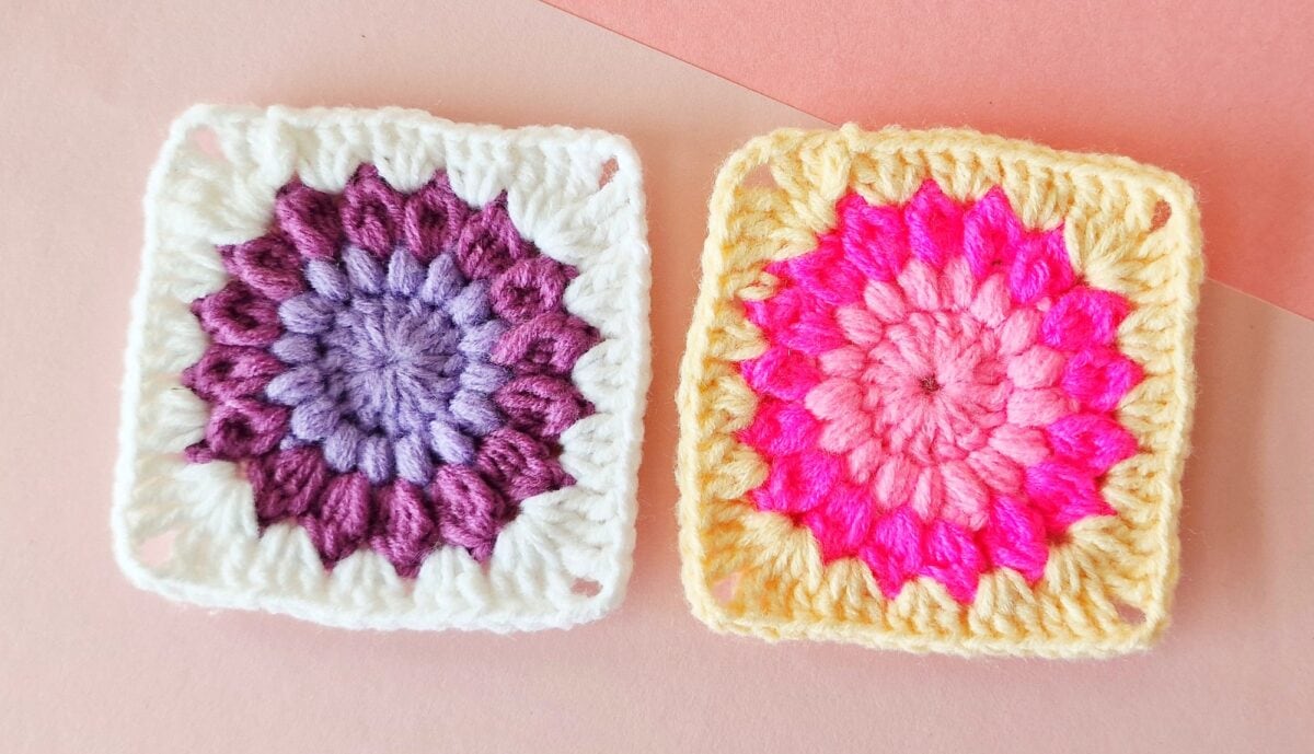 Two crocheted granny squares with flower patterns, one in purple and white, the other in pink and yellow, placed on a pink background.