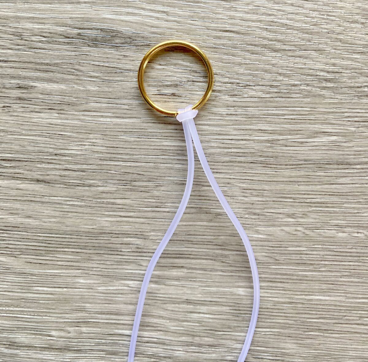 A gold metal ring lies on a wood surface with a white zip tie looped through it and fastened closed.