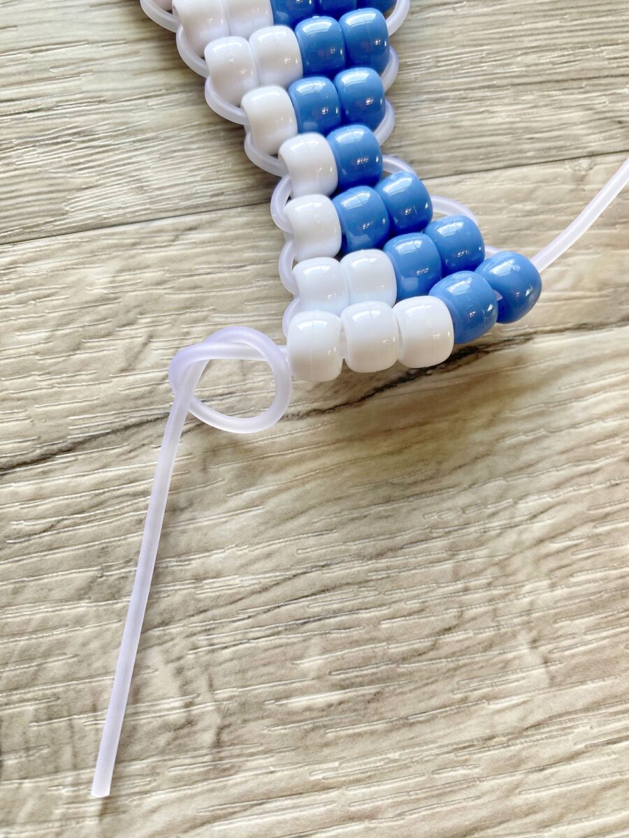 Close-up of white and blue plastic beads strung together with a plastic cord, arranged on a light wood surface.